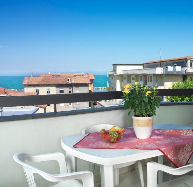 Terrazza con vista mare, tavolo bianco e pianta fiorita.