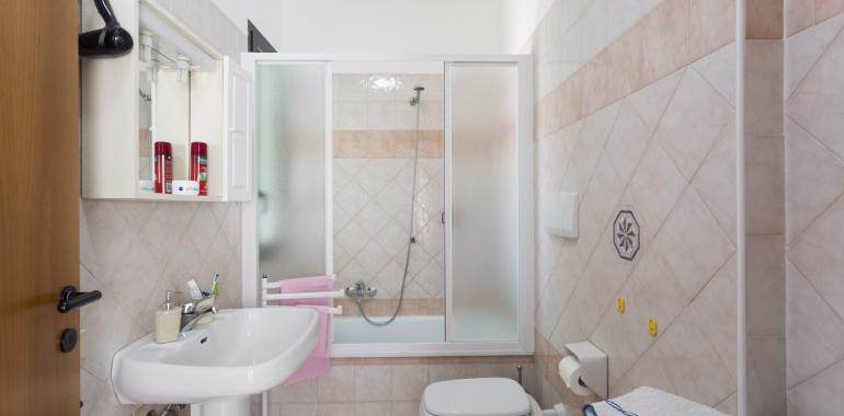 Bagno moderno con doccia, lavabo, e asciugamani rosa.