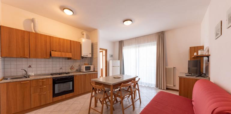 Cucina luminosa con tavolo, divano rosso e elettrodomestici moderni.