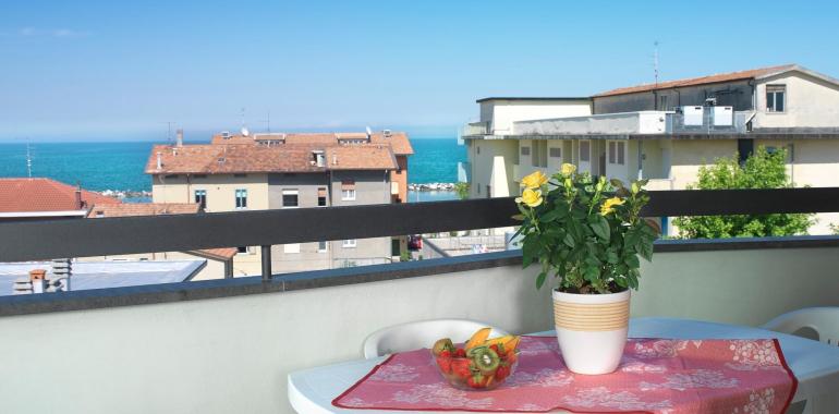 Terrazza con vista mare, tavolo bianco e pianta fiorita.